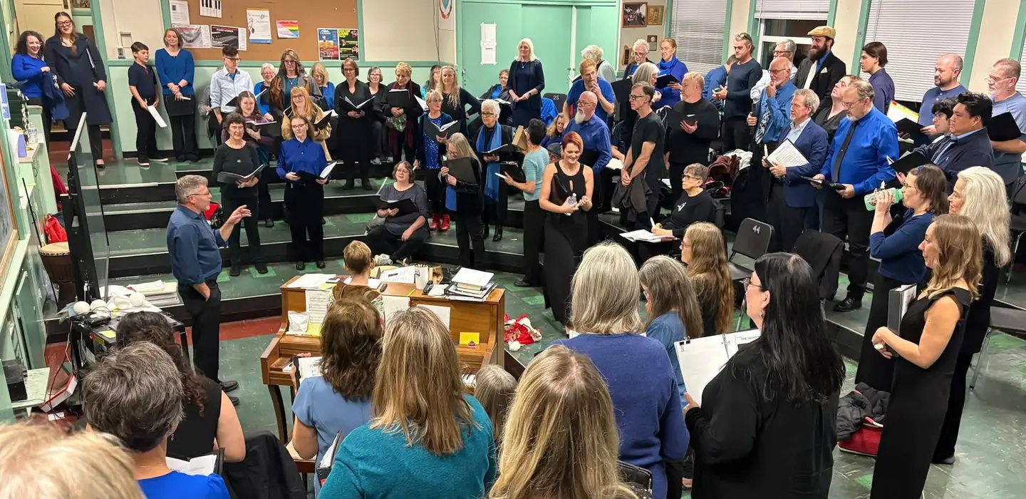Dozens of singers in concert blues rehearse around a piano in the music room.